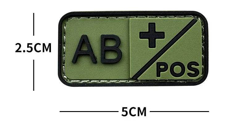 An olive green tactical patch with black border and raised black text reading 'AB' and 'POS' with a plus sign, shown with dimension lines indicating 2.5 cm height and 5 cm width on a white background.