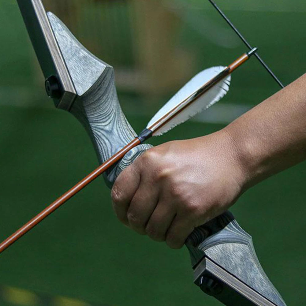 Close-up of a hand gripping a hunting recurve bow ready for shooting in an outdoor setting