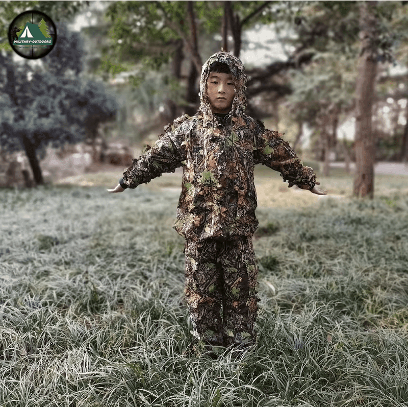 Child wearing an outdoor camouflage suit standing in grassy outdoor setting for nature activities