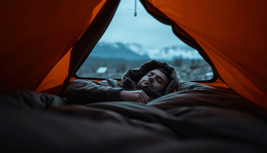 The Evolution of the Sleeping Bag shown by camper bundled in sleeping bag inside orange tent with mountain view