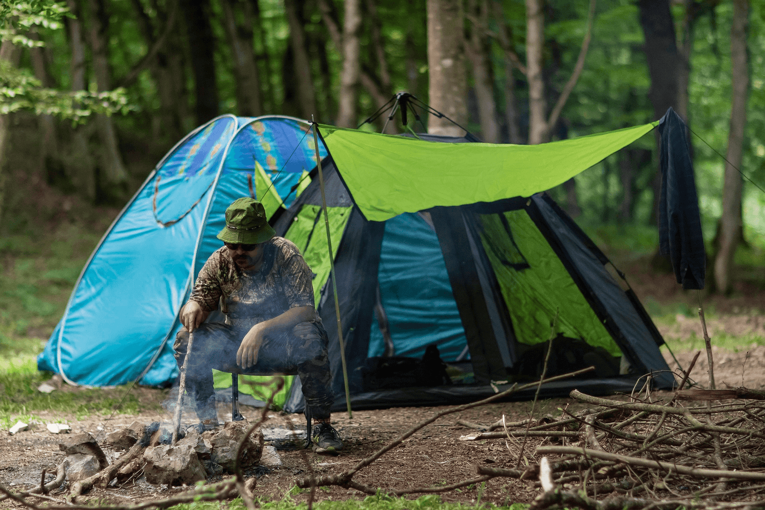 Modern camping setup with military grade tents featuring a person cooking by the fire in a wooded area