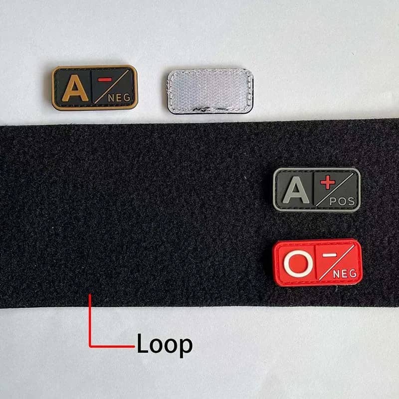 Two rectangular adhesive loop fasteners shown on a white background, one black with gold trim labeled A-NEG and one silver with a textured finish. A black hook-and-loop strip is also shown with red loop fasteners labeled A-POS and O-NEG, plus a red line and the word Loop indicating the fastener shape.