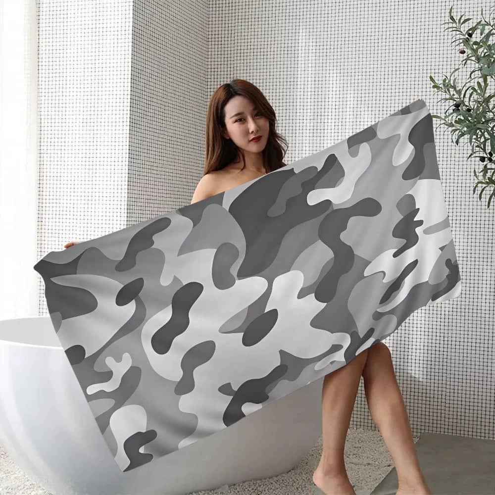 Woman holding a gray camouflage beach towel in a modern bathroom setting