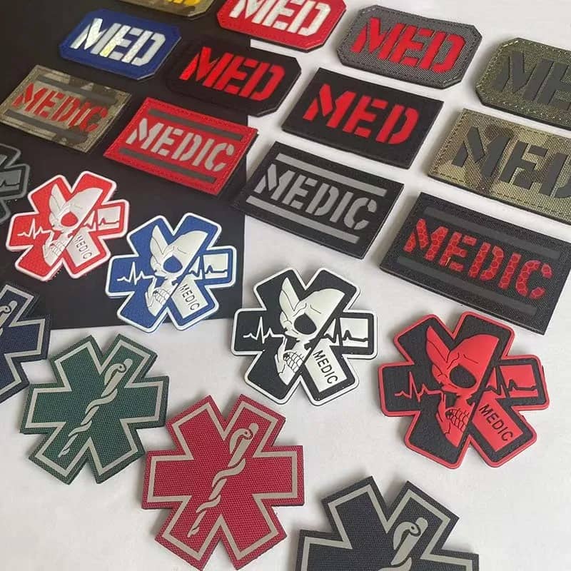 A collection of tactical medical patches featuring the word 'MEDIC' and emergency star symbols in various colors and designs, arranged on a light surface.