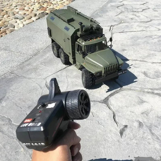 Hand holding remote control for a military RC truck on textured surface