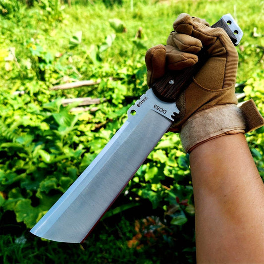 Gloved hand holding large survival knife fixed cleaver style blade with wooden handle in green outdoor setting