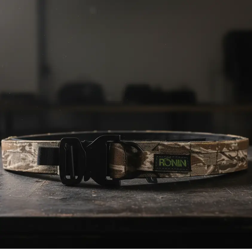 Camouflage belt with a black buckle on a white surface, blurred background